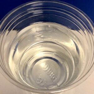 Clear plastic Dixie cup 3/4 filled with water in the center of the photo. The cup is sitting on a white countertop with a cobalt blue painted wall in the background.