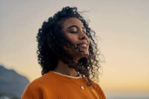 Relaxed woman with a smile of relief on her face wearing orange sweater with curly hair.